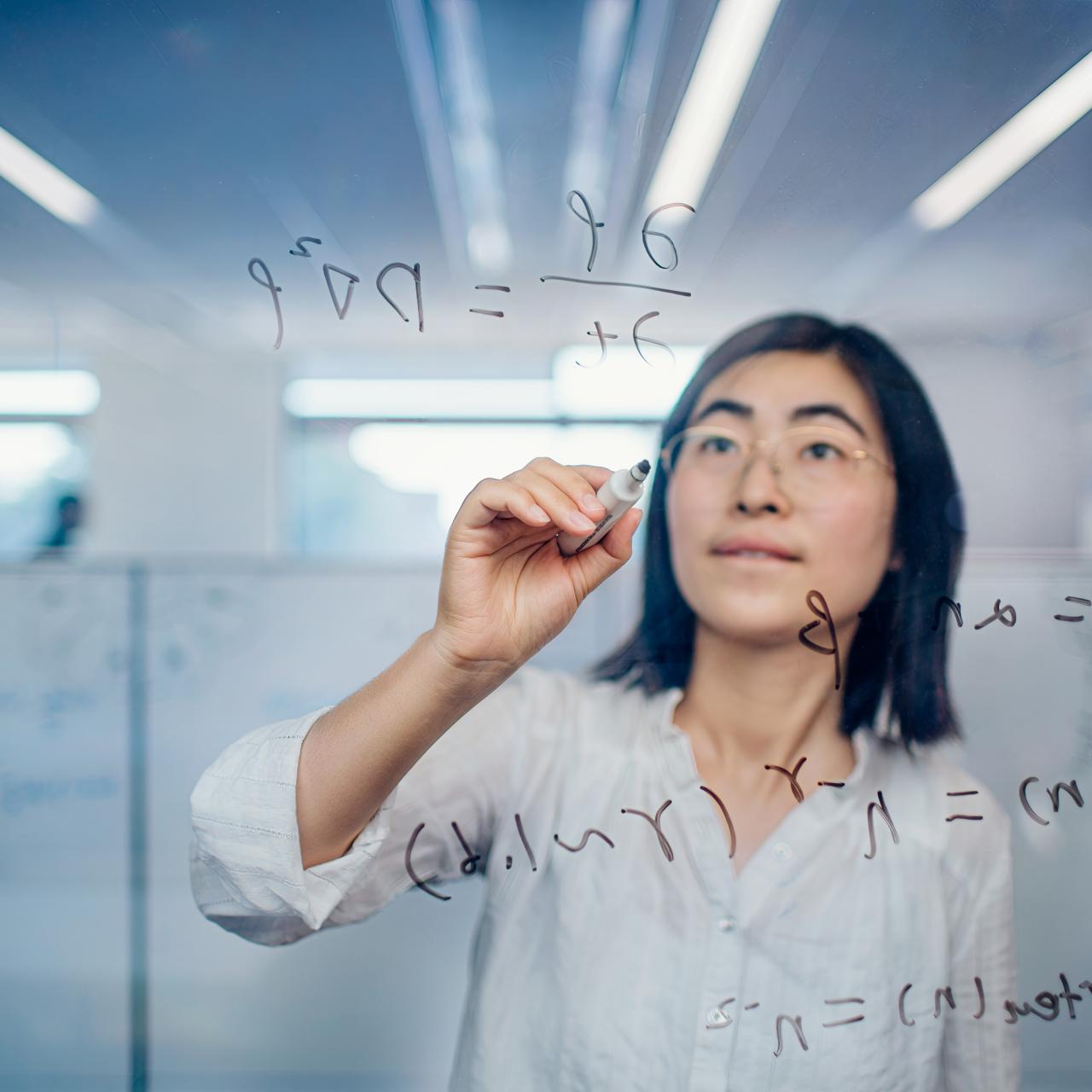 Researcher writing a formula on a glass board.