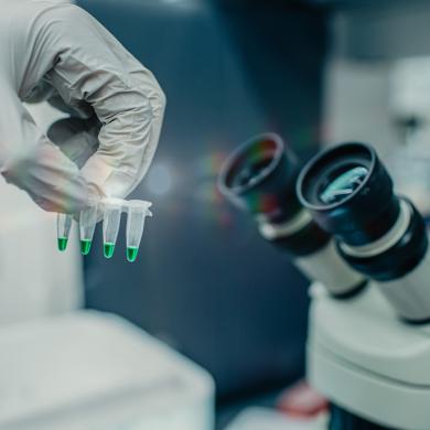 Closeup of a research holding pipettes next to a microscope