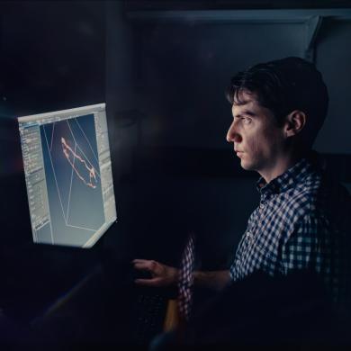 Researcher reviewing microscope results on a computer screen in a dark room