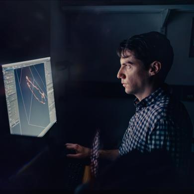 Researcher reviewing microscope results on a computer screen in a dark room