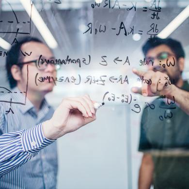 Two researchers working on an equation on a glass board