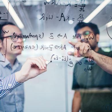 Two researchers working on an equation on a glass board